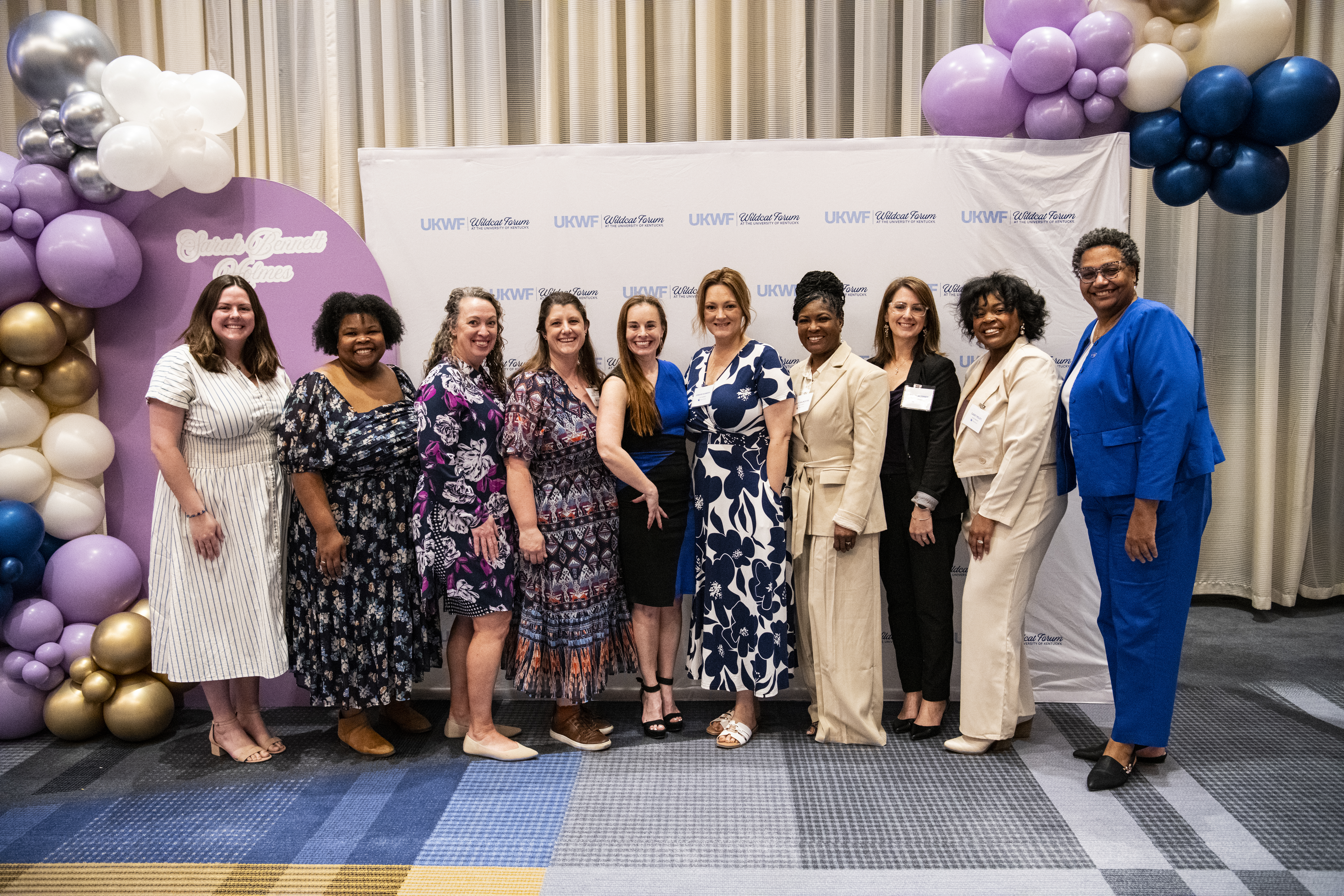 UKWF board members, ten women, posing against a colorful background. 